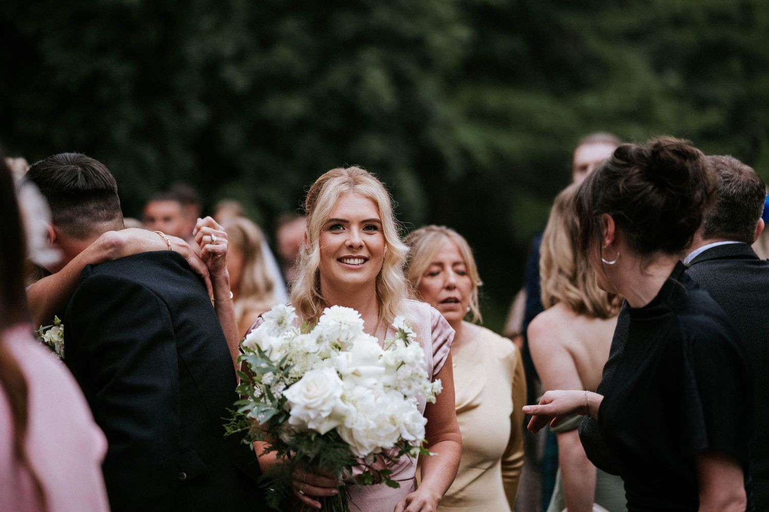 Wedding guests gather outdoors for candid moments surrounded by lush greenery and natural light.
