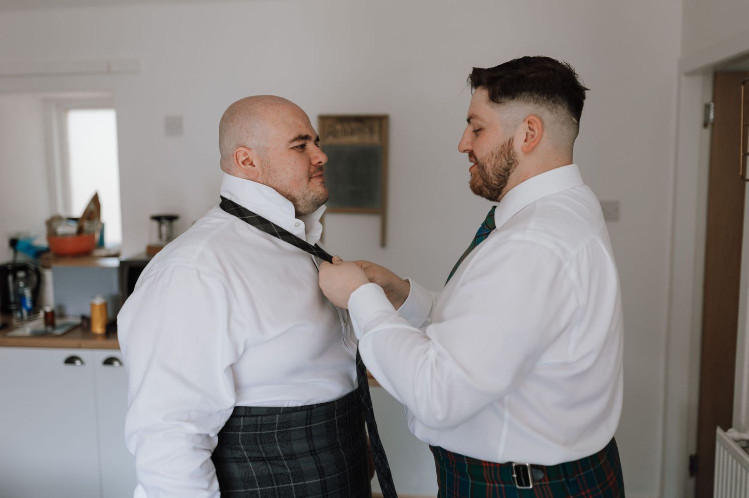 Two people in formal white shirts helping with bow tie adjustments.