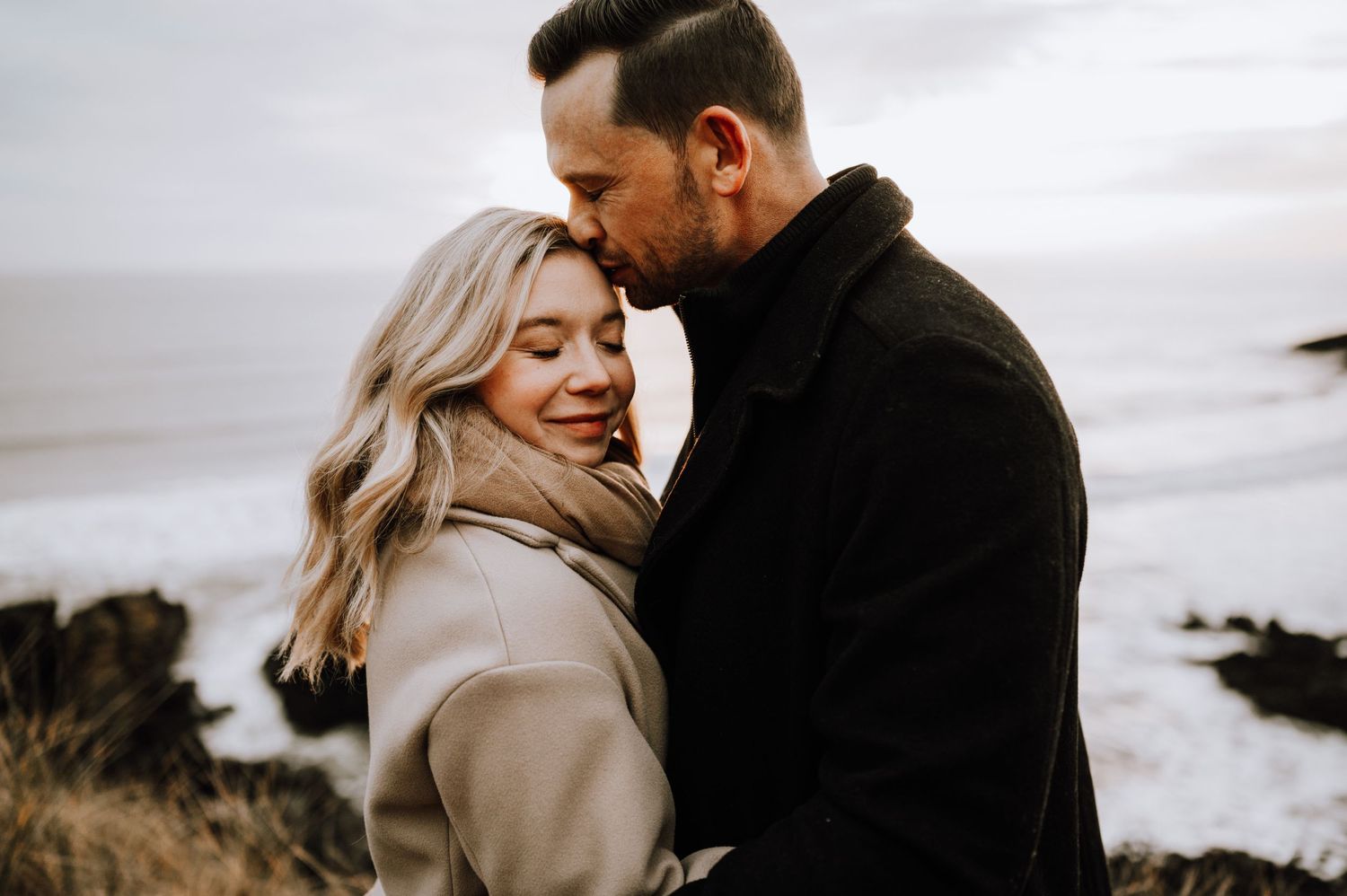 Joyful couple sharing a laugh while embracing on a coastal clifftop.