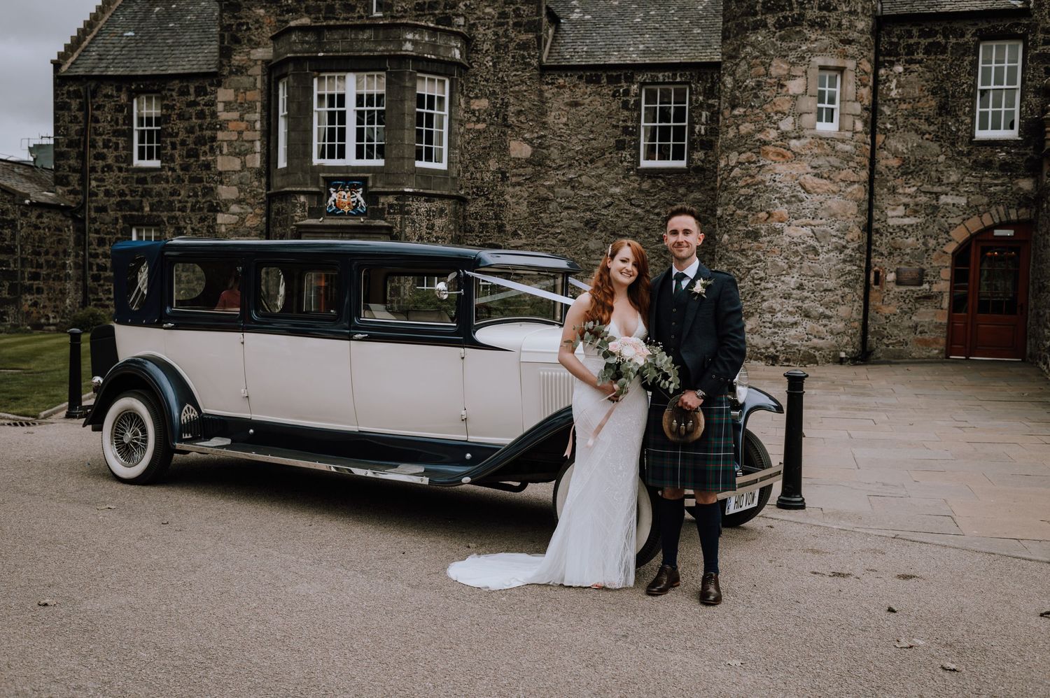 Classic white vintage wedding car parked in front of a stone Scottish castle.