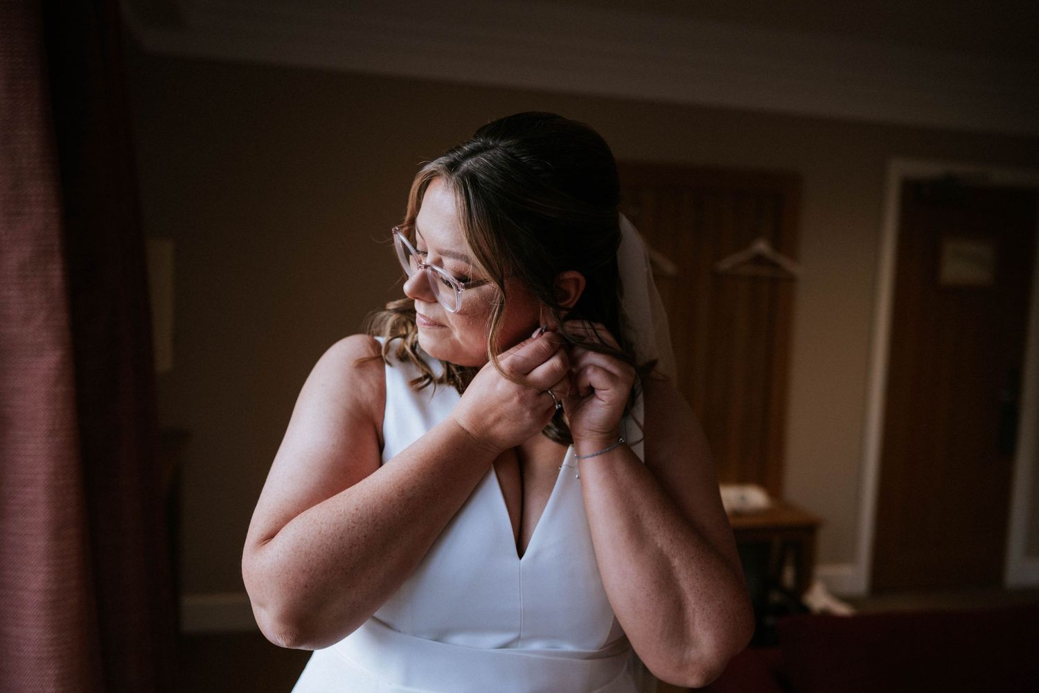 A bride in a white dress puts on earrings while getting ready for her wedding day.
