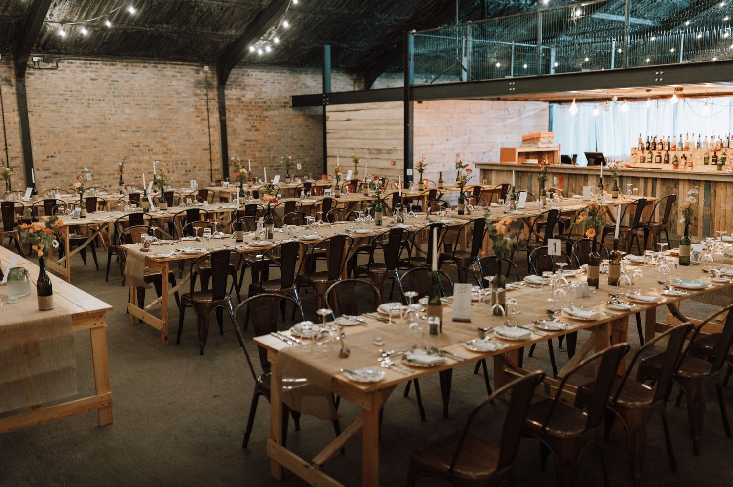 Reception venue with rustic wooden tables and chairs set for wedding dinner in industrial space.