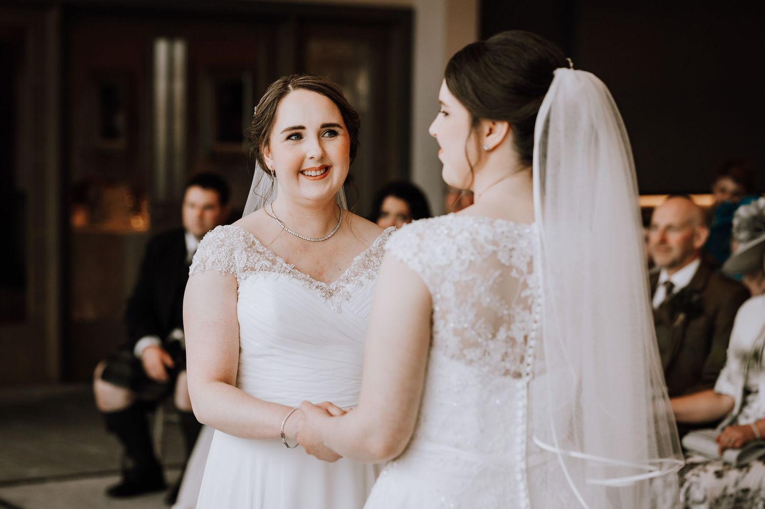 Wedding guests dressed in formal attire seated in rows during an indoor ceremony.