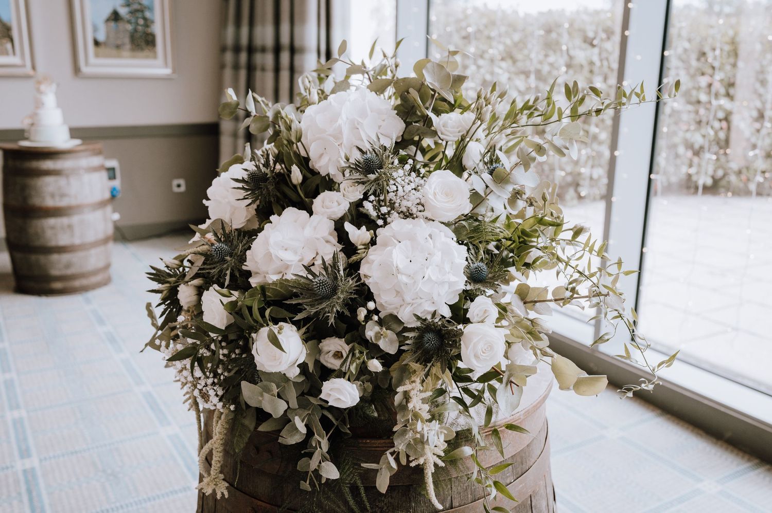Elegant white floral wedding centerpiece arrangement with roses and greenery by a window.
