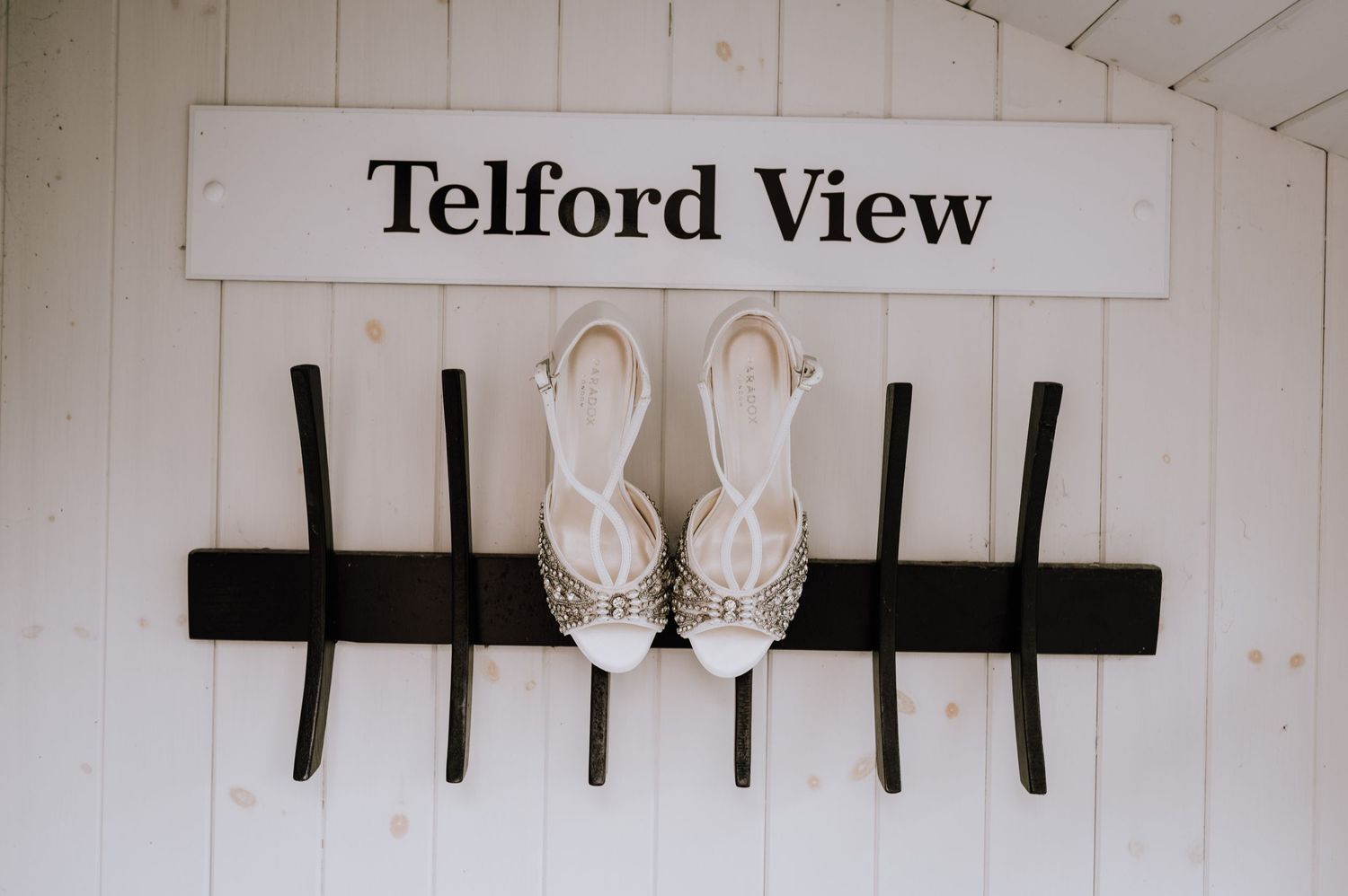 White bridal shoes displayed on black hooks under a Telford View sign.