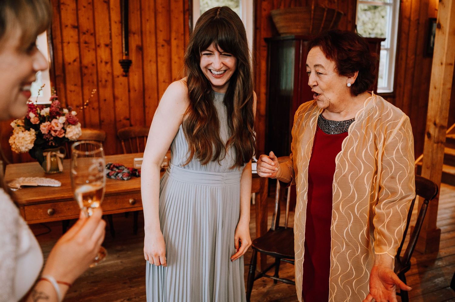 Three women share a candid moment of laughter in a wood-paneled room.