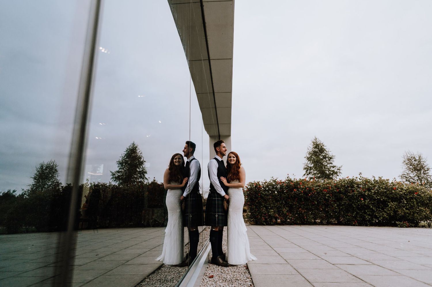 A wedding party poses for a creative reflection shot outside on a modern terrace.