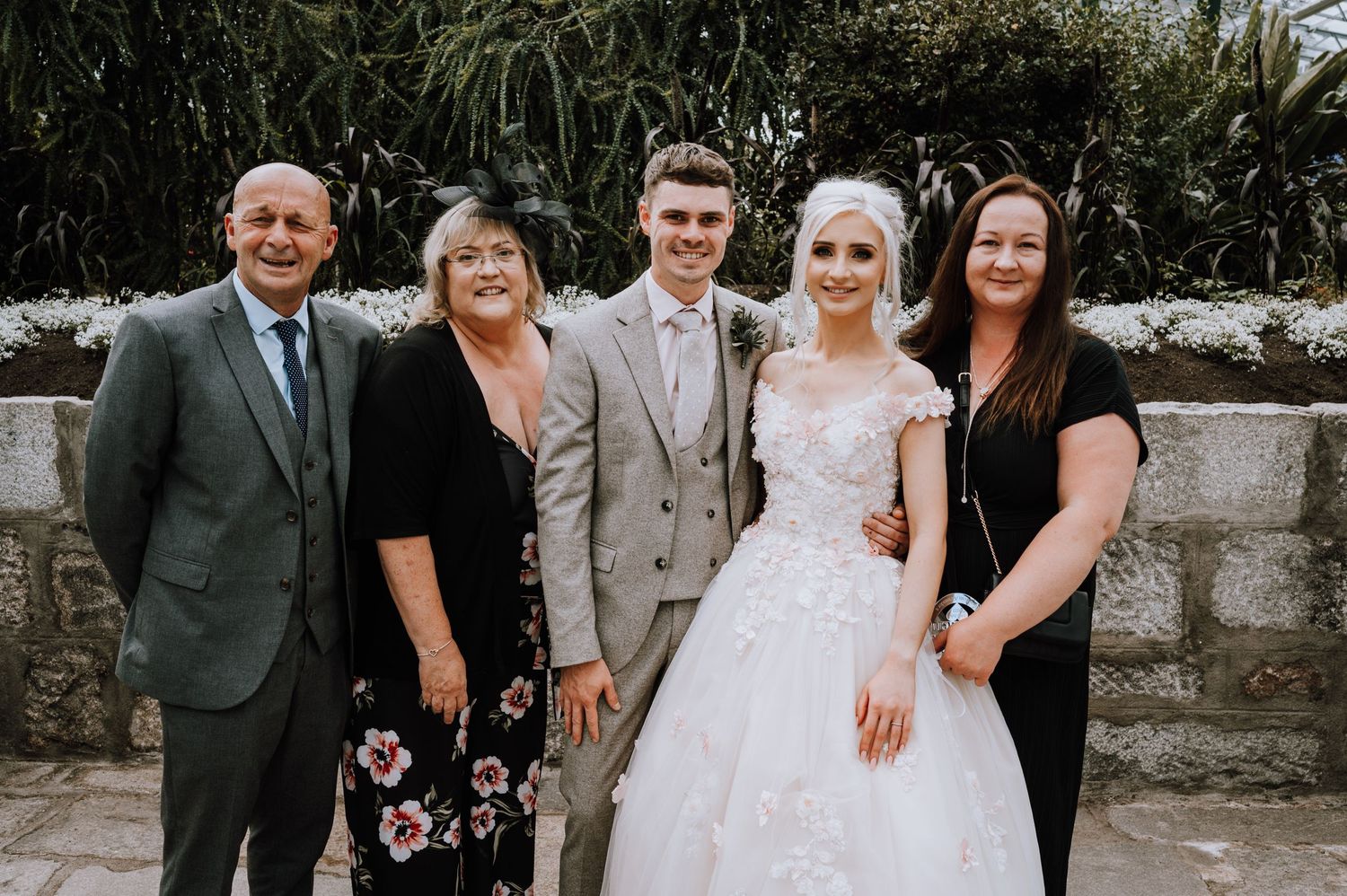 A small wedding group poses together against a stone wall backdrop.