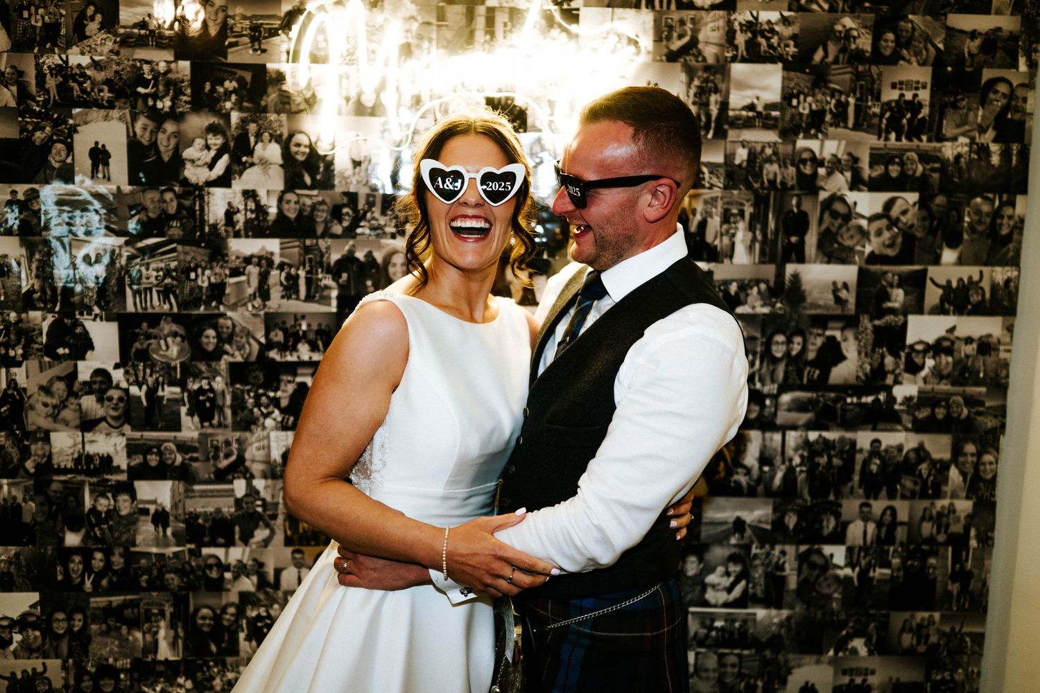 Joyful dance celebration against a black and white photo collage wall at wedding reception.