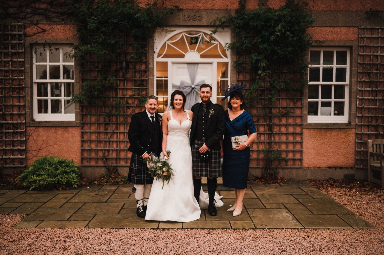 Wedding party poses in front of a classic brick building with ivy-covered walls.