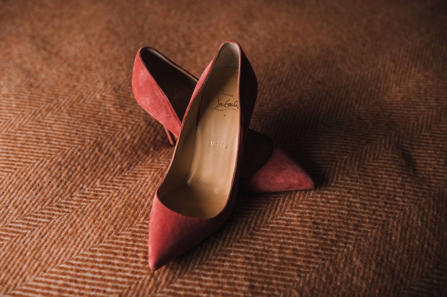 Pair of pink suede high heel shoes on a textured brown fabric surface.