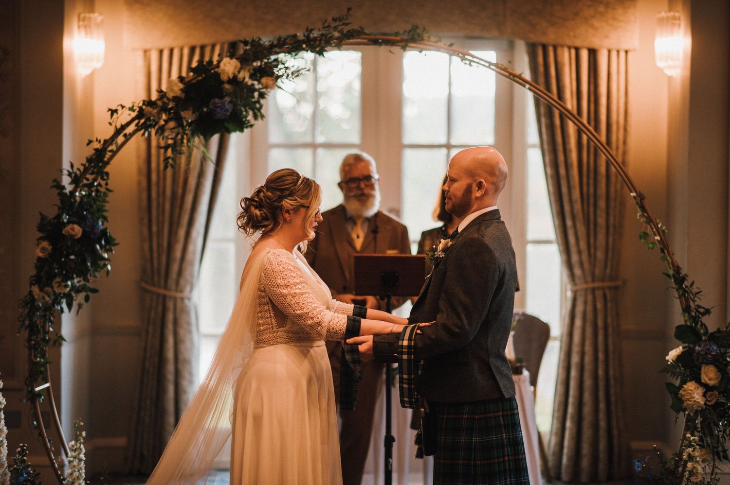 Couple exchanging vows beneath an ornate floral arch during their wedding ceremony.