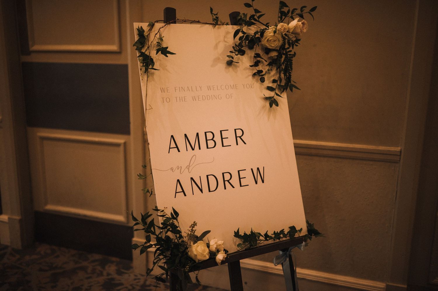 Wedding welcome sign for Amber and Andrew decorated with greenery on an elegant easel.