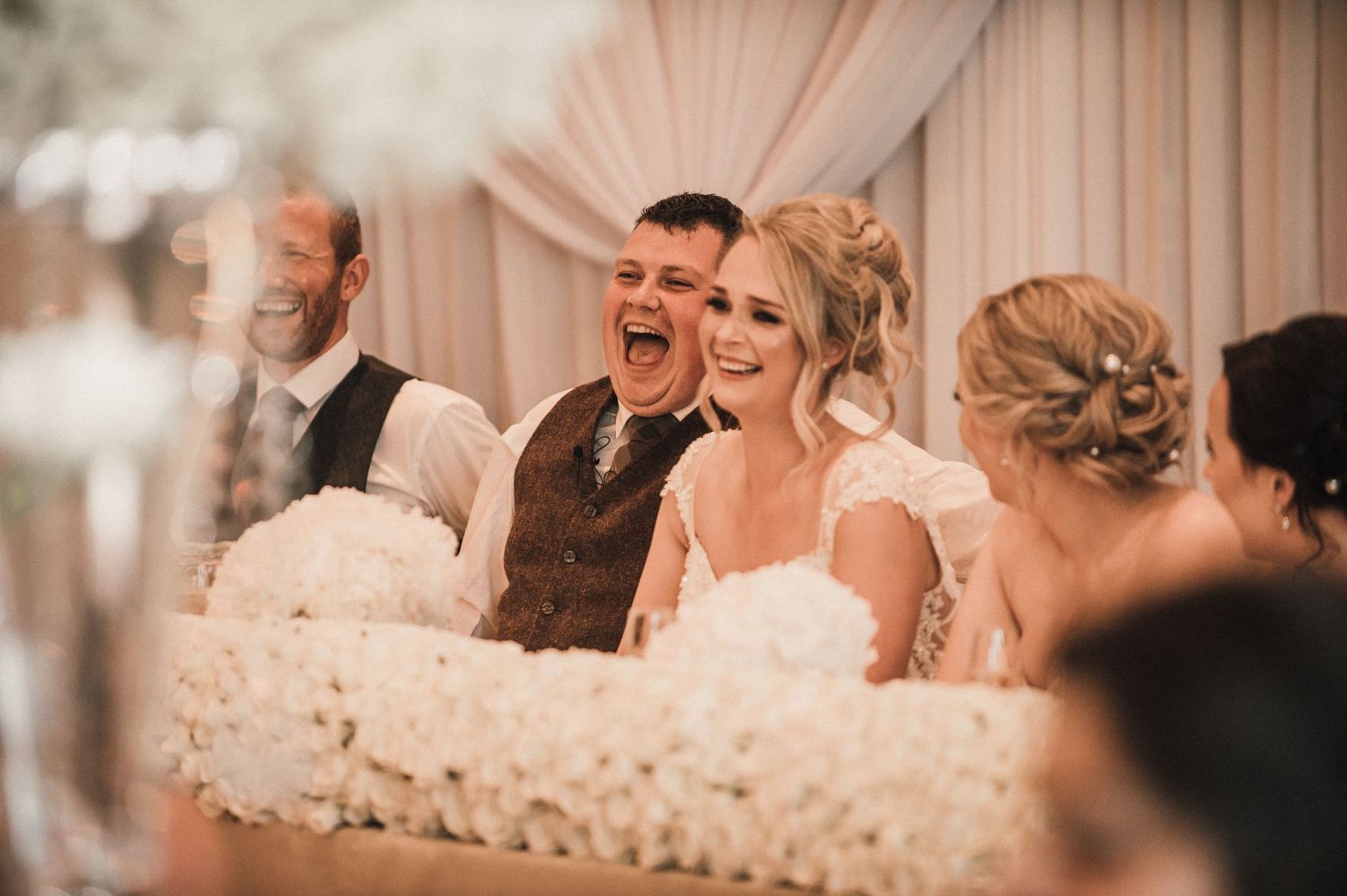 Wedding party members share genuine laughter during reception toasts.