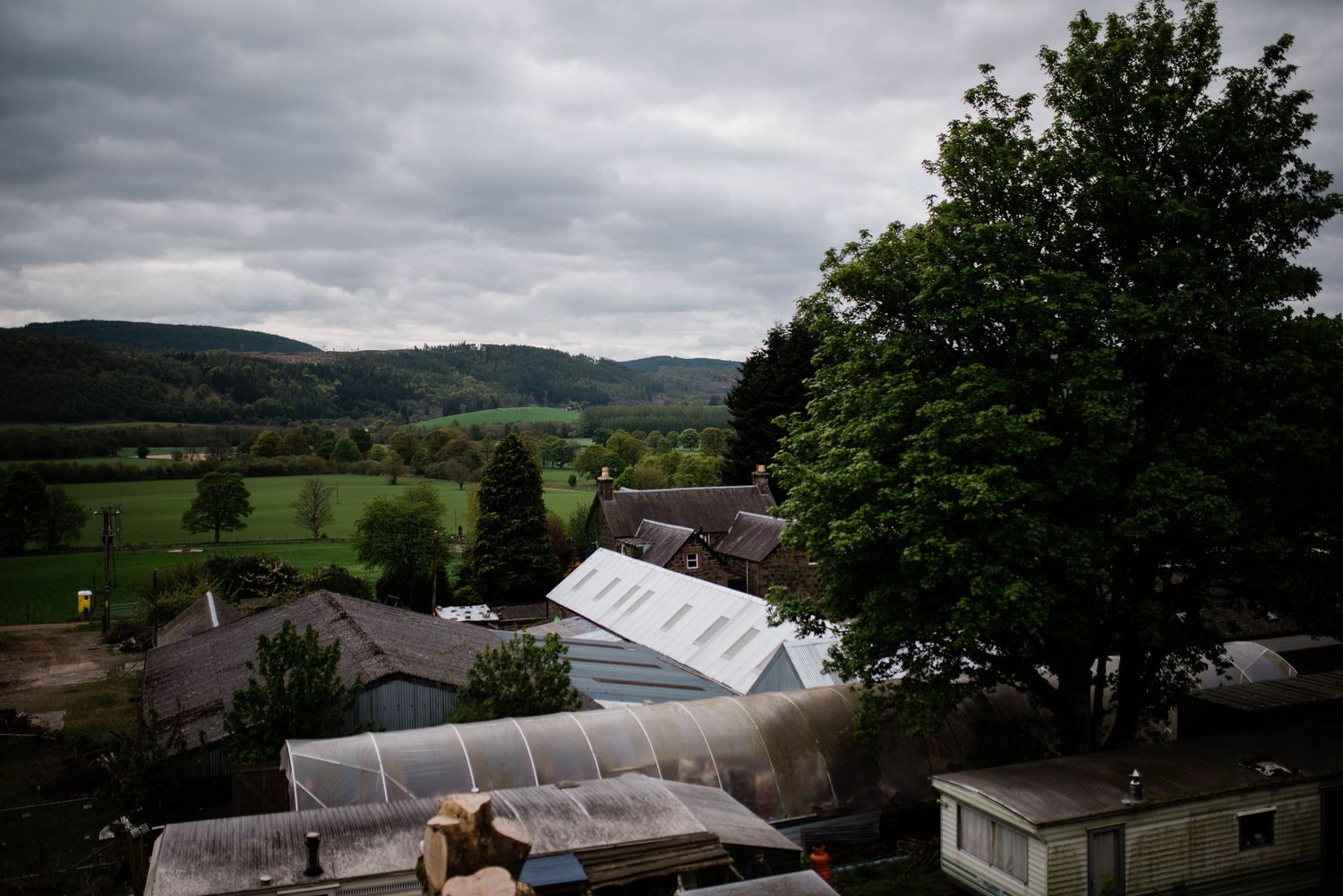 Aerial view of a wedding venue tent surrounded by green countryside and mountains under cloudy skies.