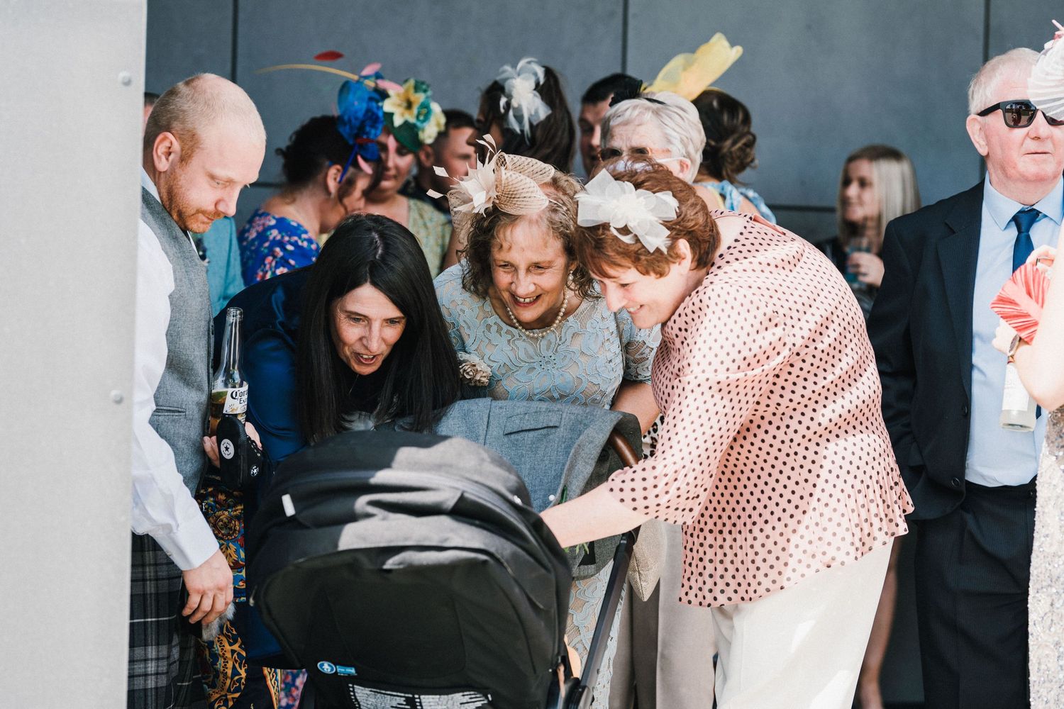Wedding guests gather around baby stroller at outdoor reception event.