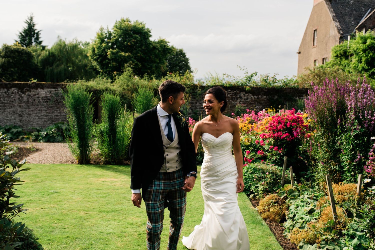 A couple walks through a vibrant garden filled with colorful flowers on their wedding day.