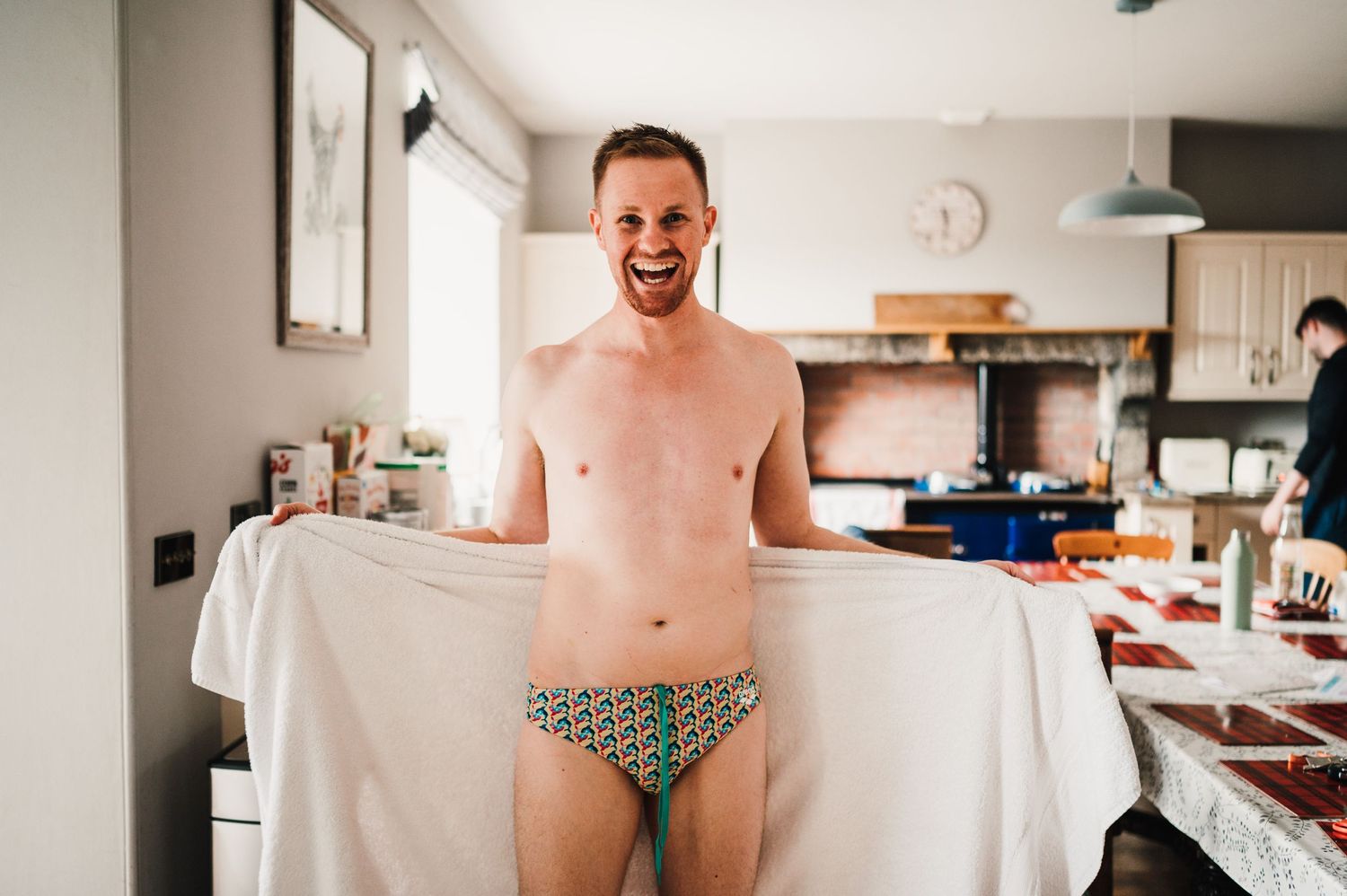 Person standing in kitchen wearing minimal attire and holding up white fabric.