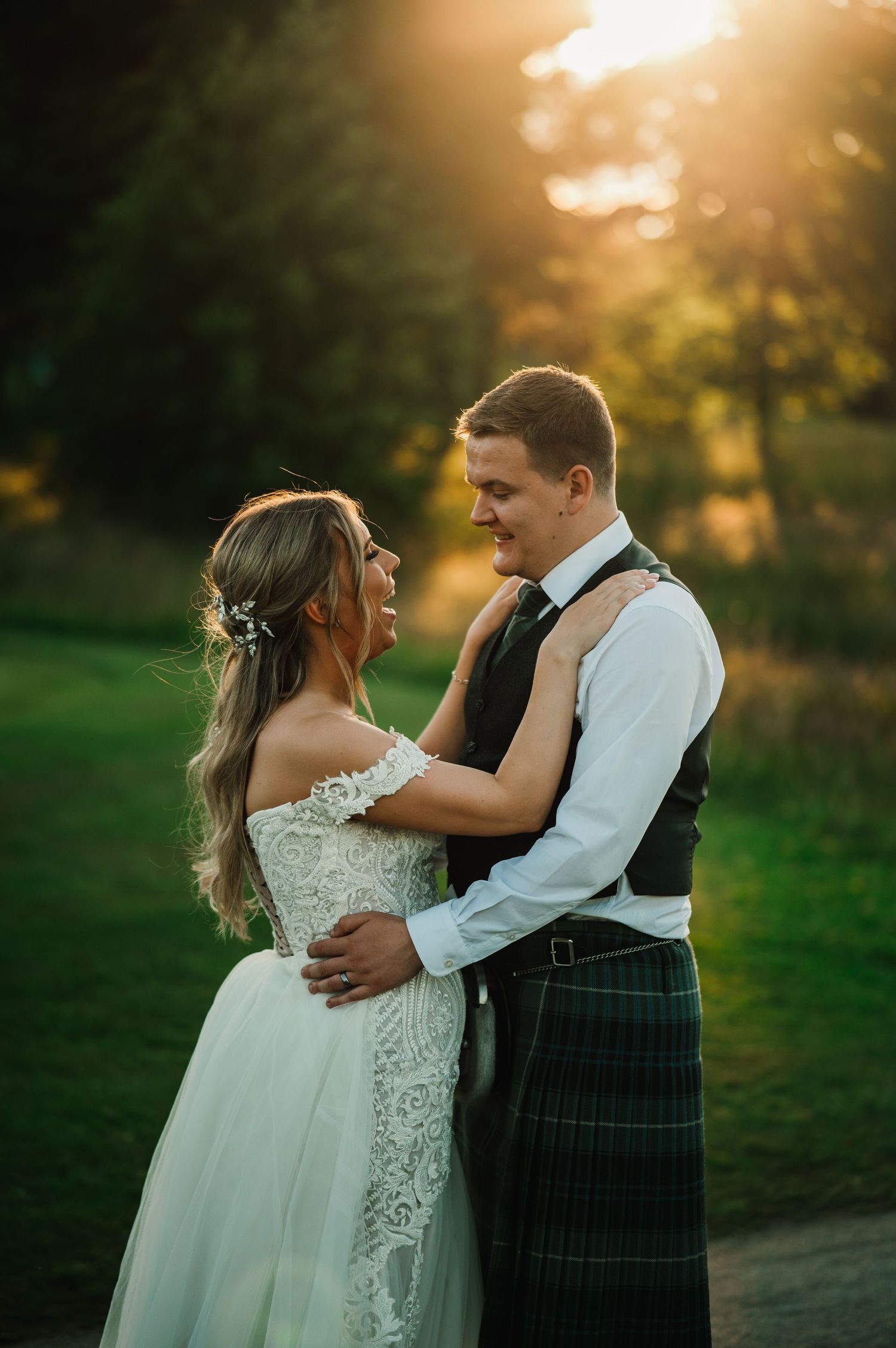 A couple embraces on a golf course path during golden hour with the groom wearing a traditional kilt.