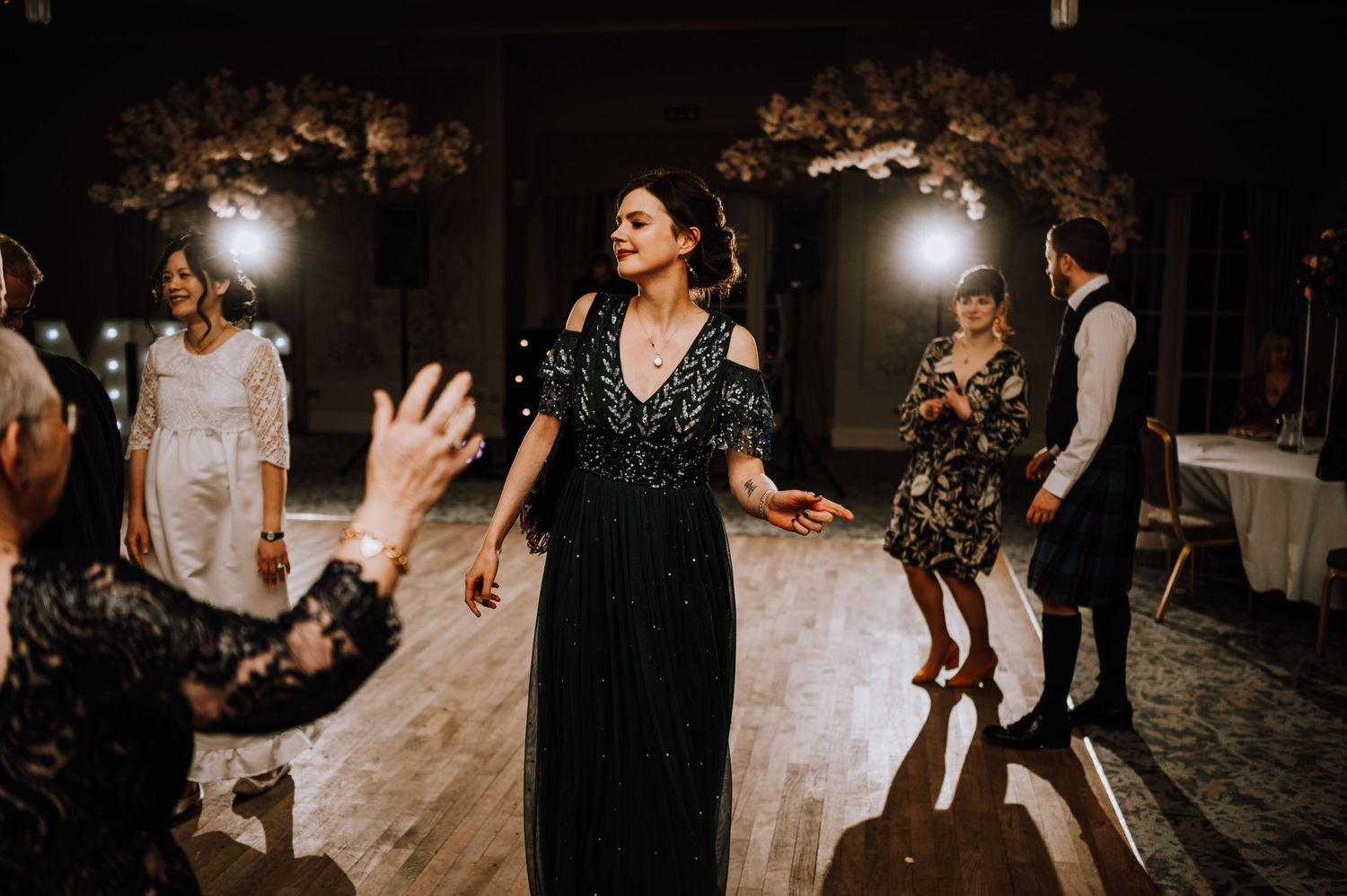 People dancing at a wedding reception with moody lighting and decorative elements in the background.
