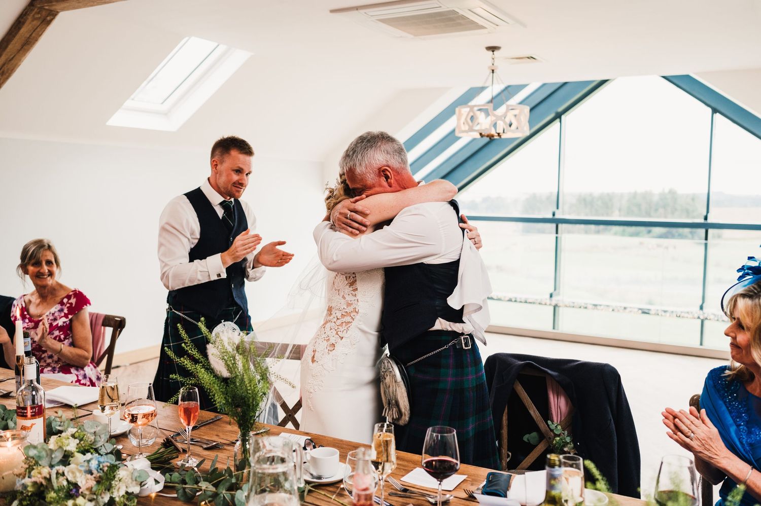 Emotional moment during wedding speeches as guests embrace at a seaside venue.