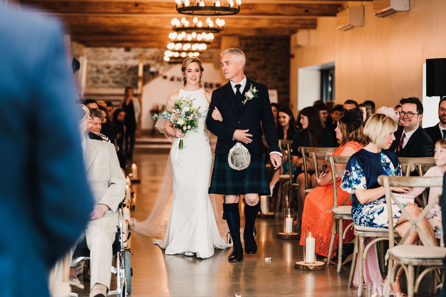 Wedding ceremony processional featuring traditional Scottish attire in an elegant indoor venue.