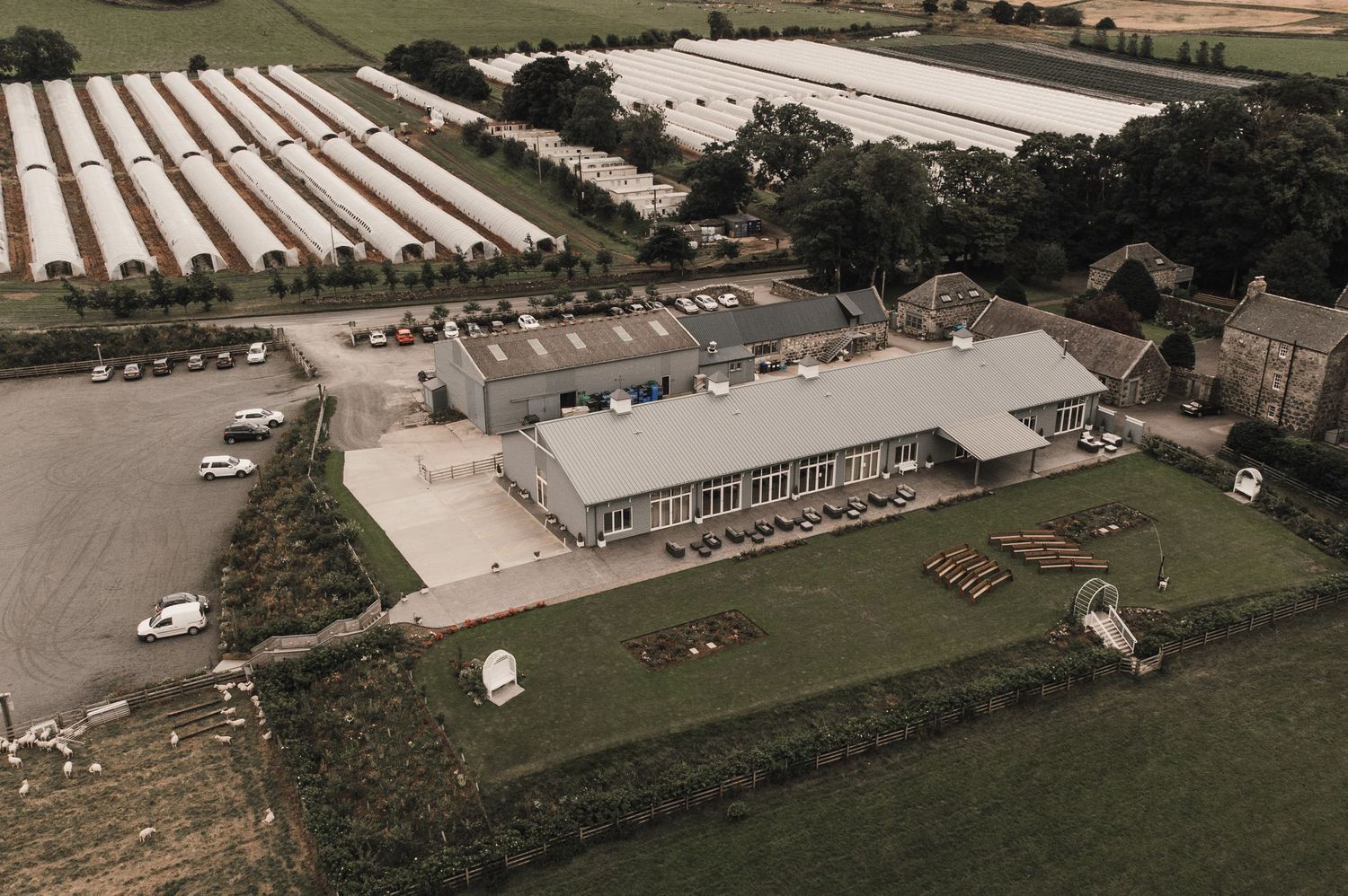 Aerial view of a large venue building surrounded by parking lots and greenhouse structures.