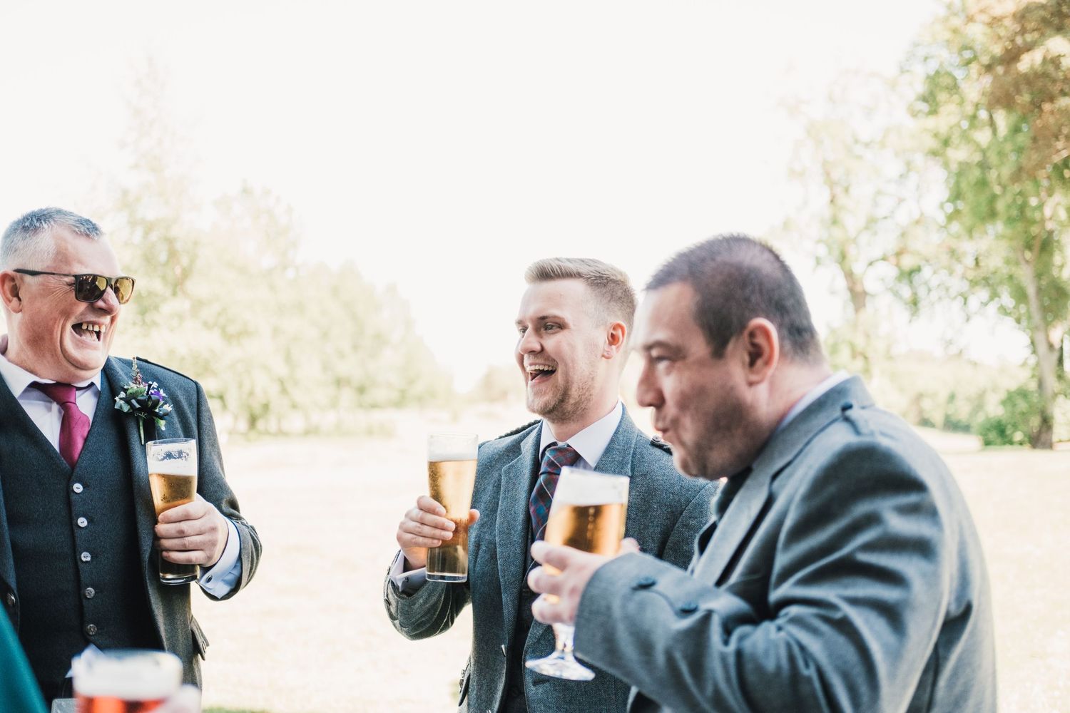 Guests enjoy drinks and laughter during an outdoor wedding reception.