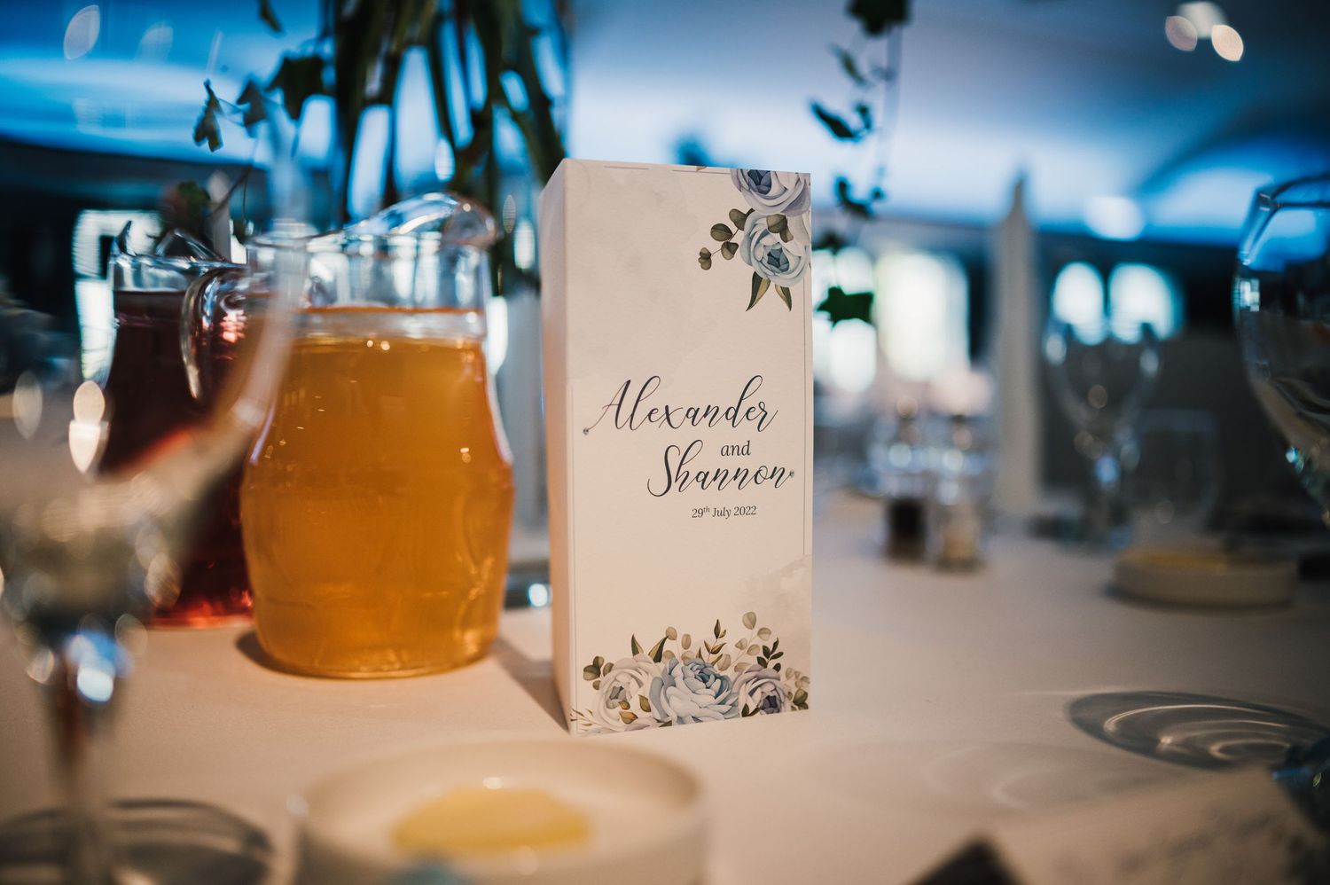 Wedding reception table setting with menu card and glass of beer in ambient lighting.