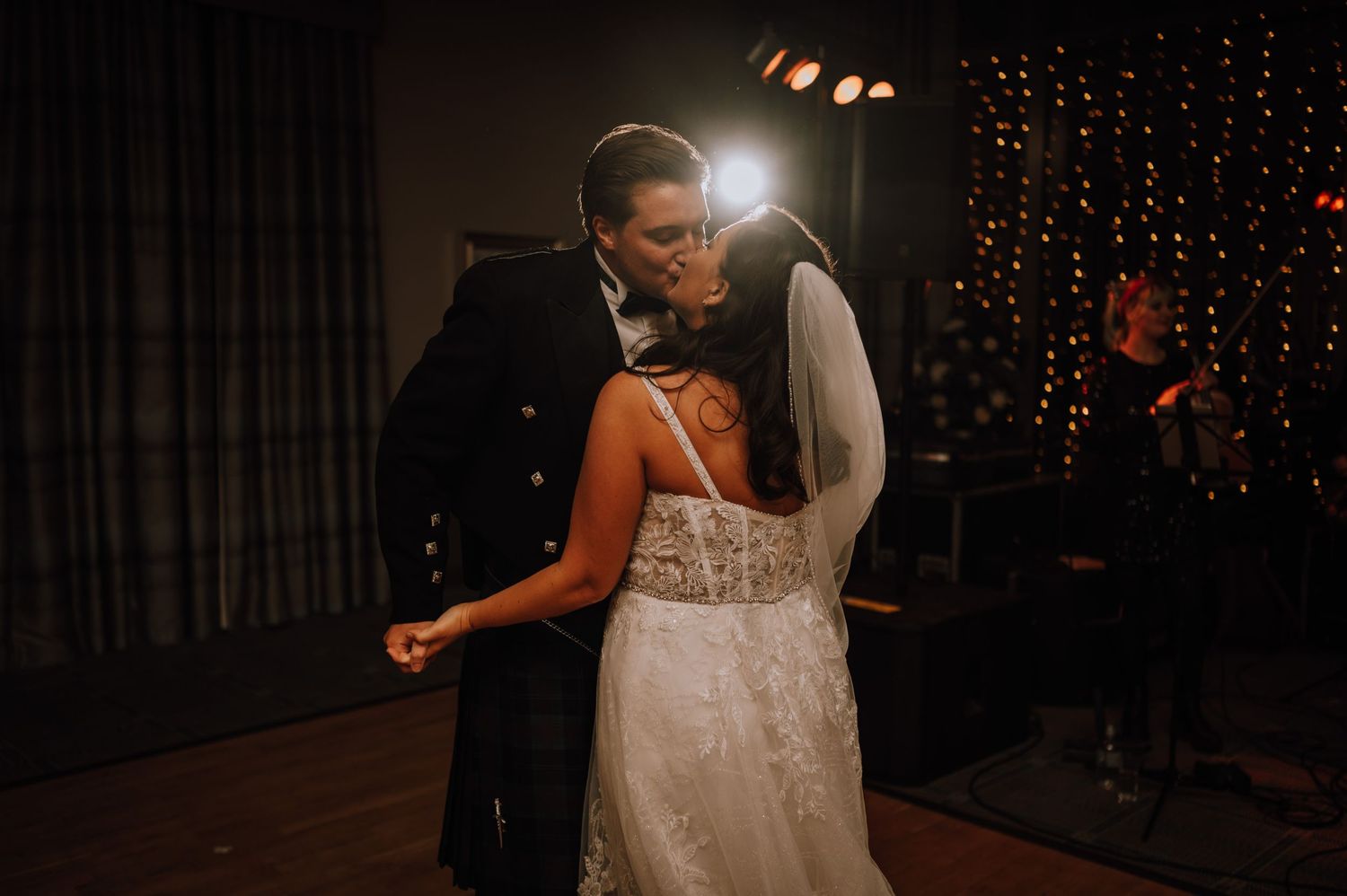 Couple shares intimate dance moment during wedding reception with string lights glowing.
