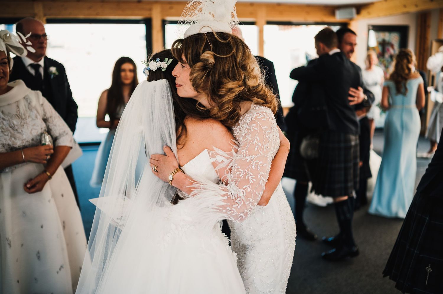 Two figures in white dresses share an intimate embrace during wedding celebration.