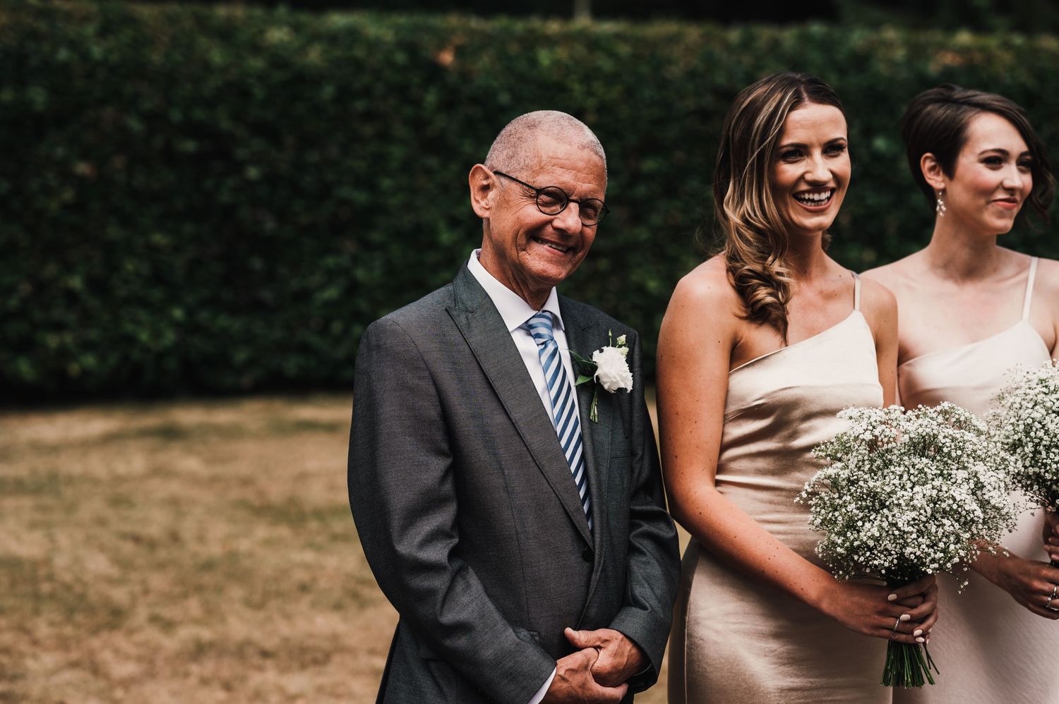 Wedding party members in champagne dresses with baby's breath bouquets posing in garden setting.