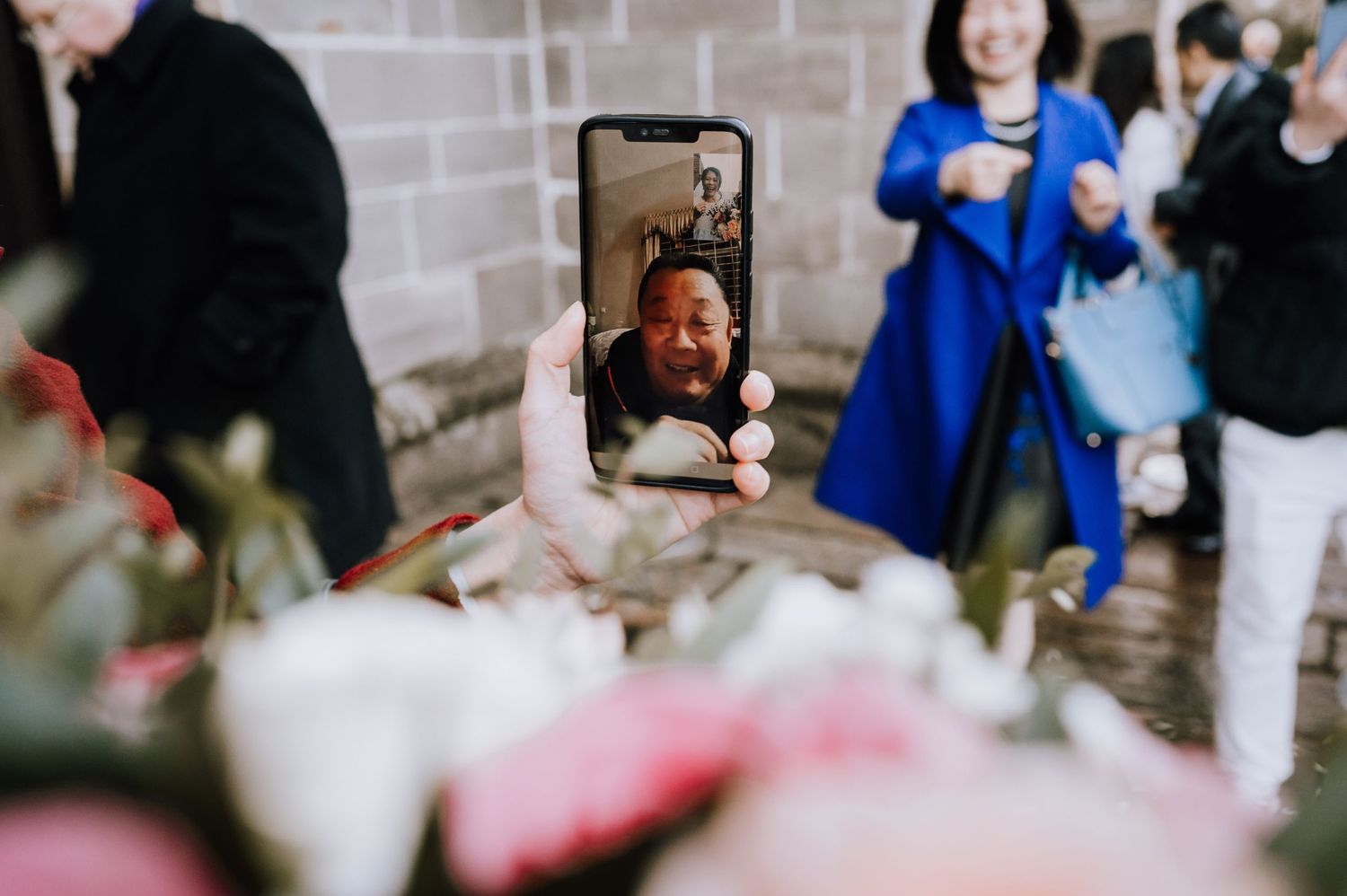A mobile phone captures a reflection in a mirror surrounded by pink and white flowers.