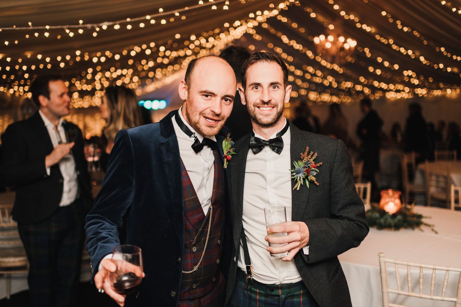 Wedding guests sharing a celebratory moment under string lights at an indoor reception.