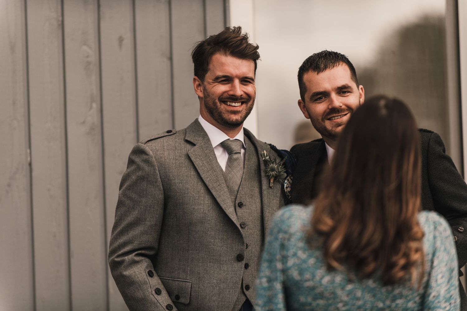 Wedding guests smile and chat during an informal moment at a rustic outdoor venue.