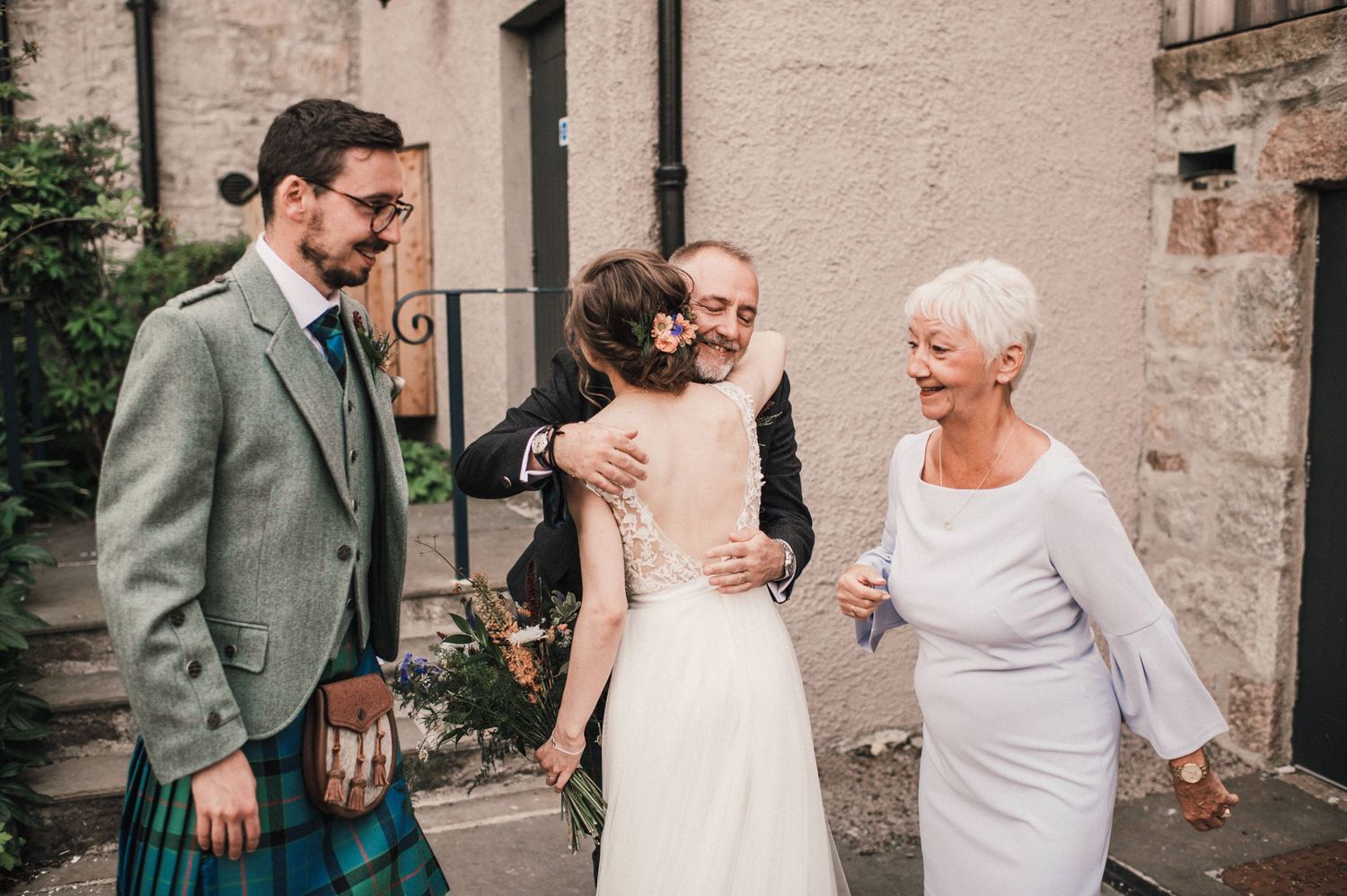 Joyful wedding celebration moments outside a traditional Scottish stone building.