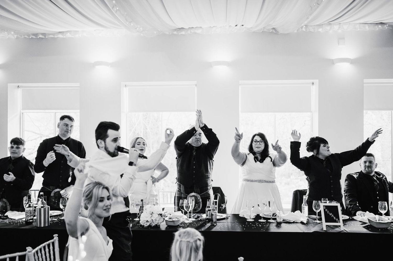 Logie House Wedding Photography. Black and white image of wedding reception guests celebrating with raised arms.