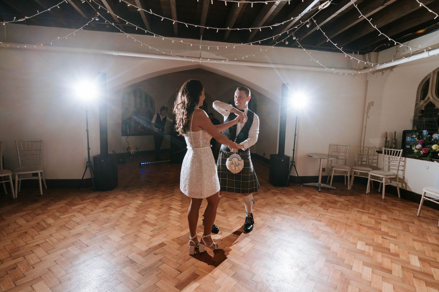 A couple spins and dances together in a reception hall under twinkling lights.