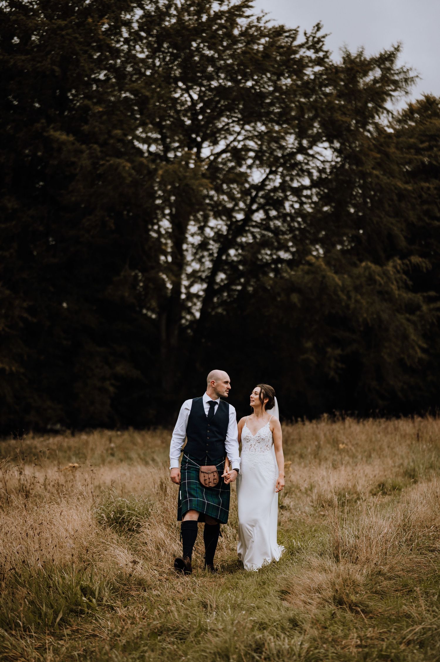 Aberdeen Wedding Photography. Couple walking through a golden field with Scottish highland wedding attire.