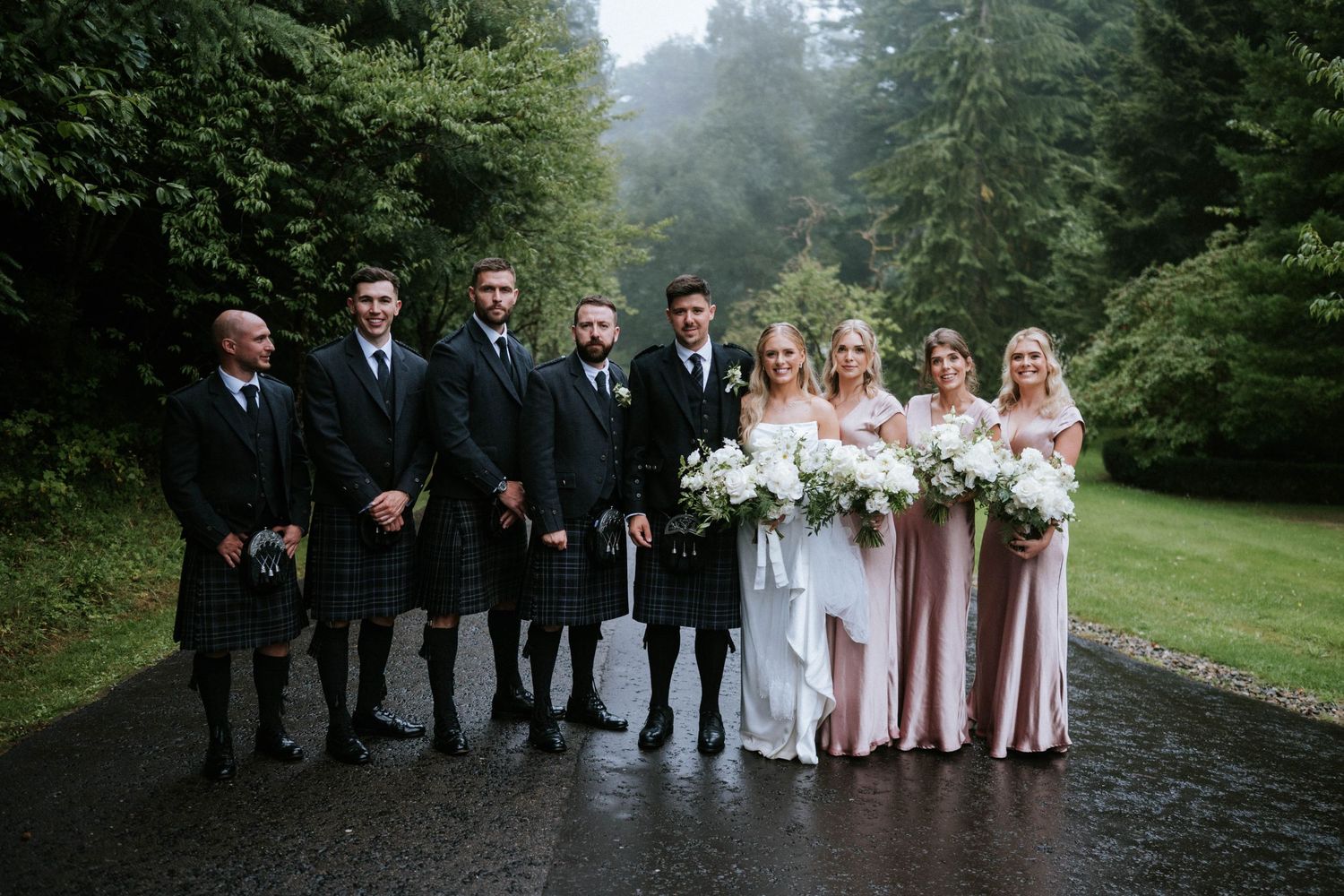 Wedding party lined up on a misty forest path for formal photographs.