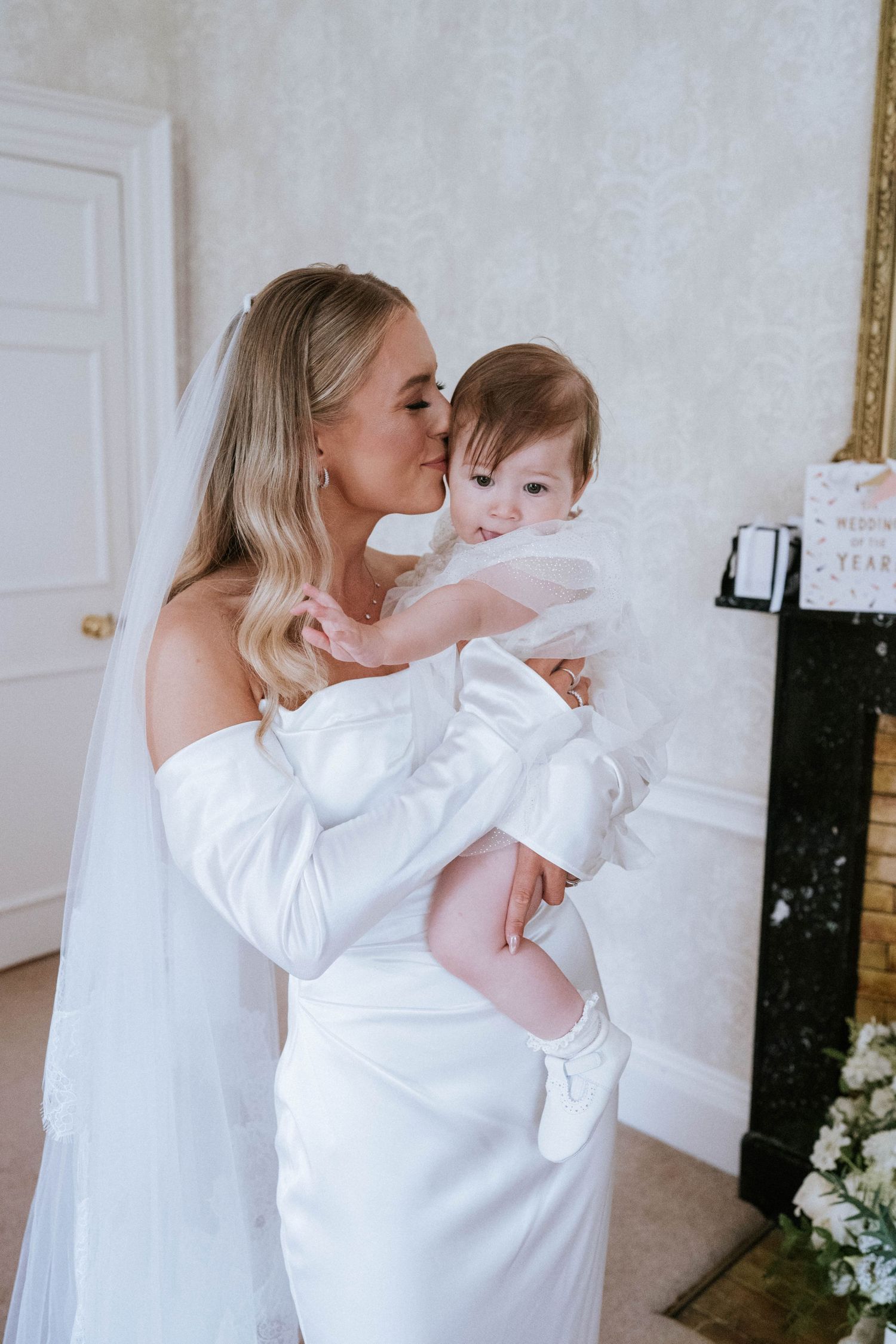 Two people in white outfits sharing a tender moment against a light background.