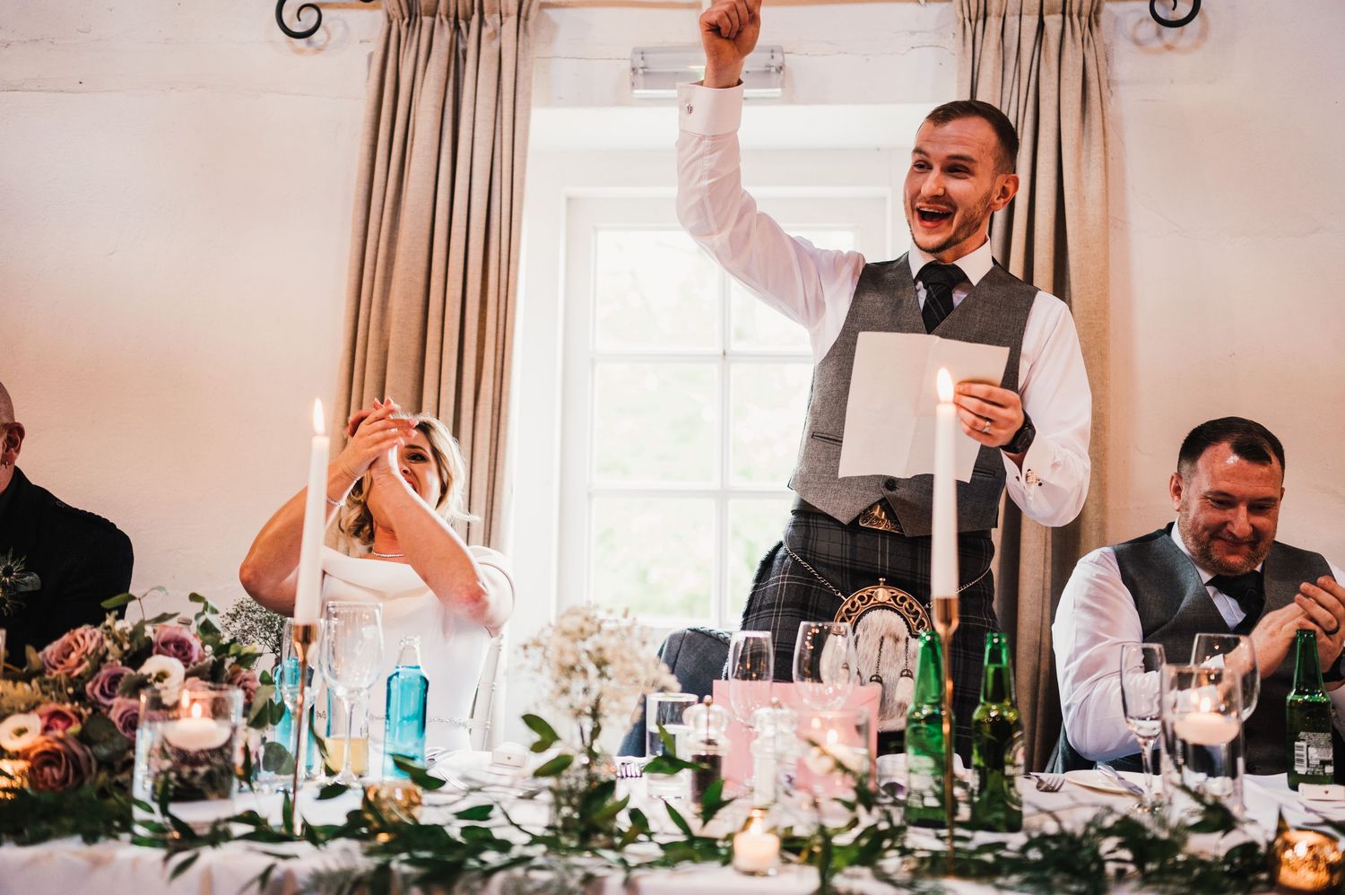 Wedding reception speech moment with guests celebrating at a decorated banquet table.