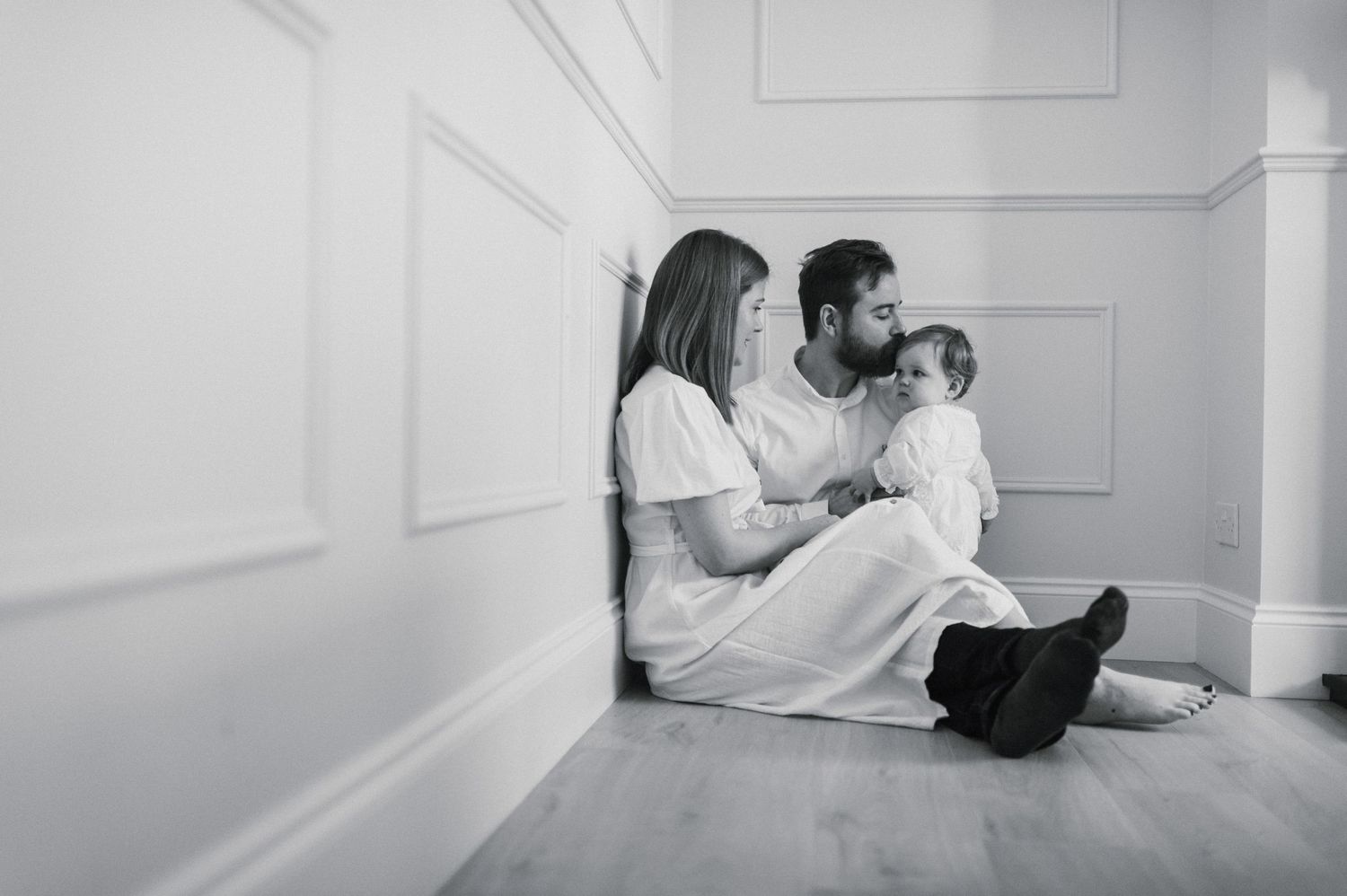 A couple sits together on the floor against a white wall in a minimalist setting.