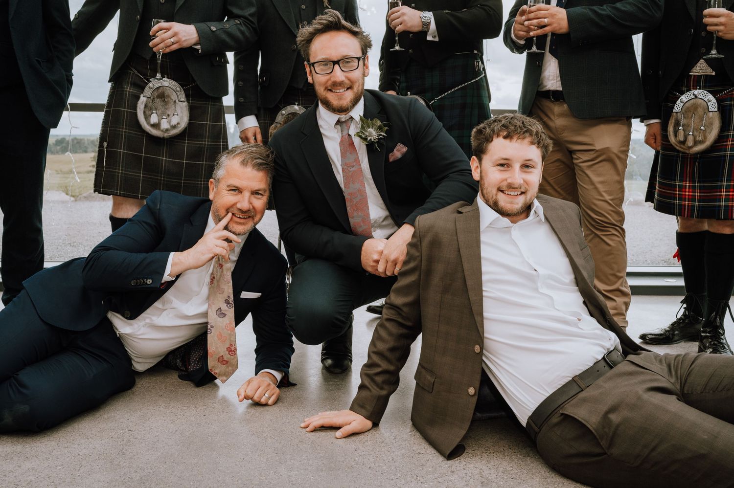 Groomsmen in kilts relaxing and posing casually on floor.