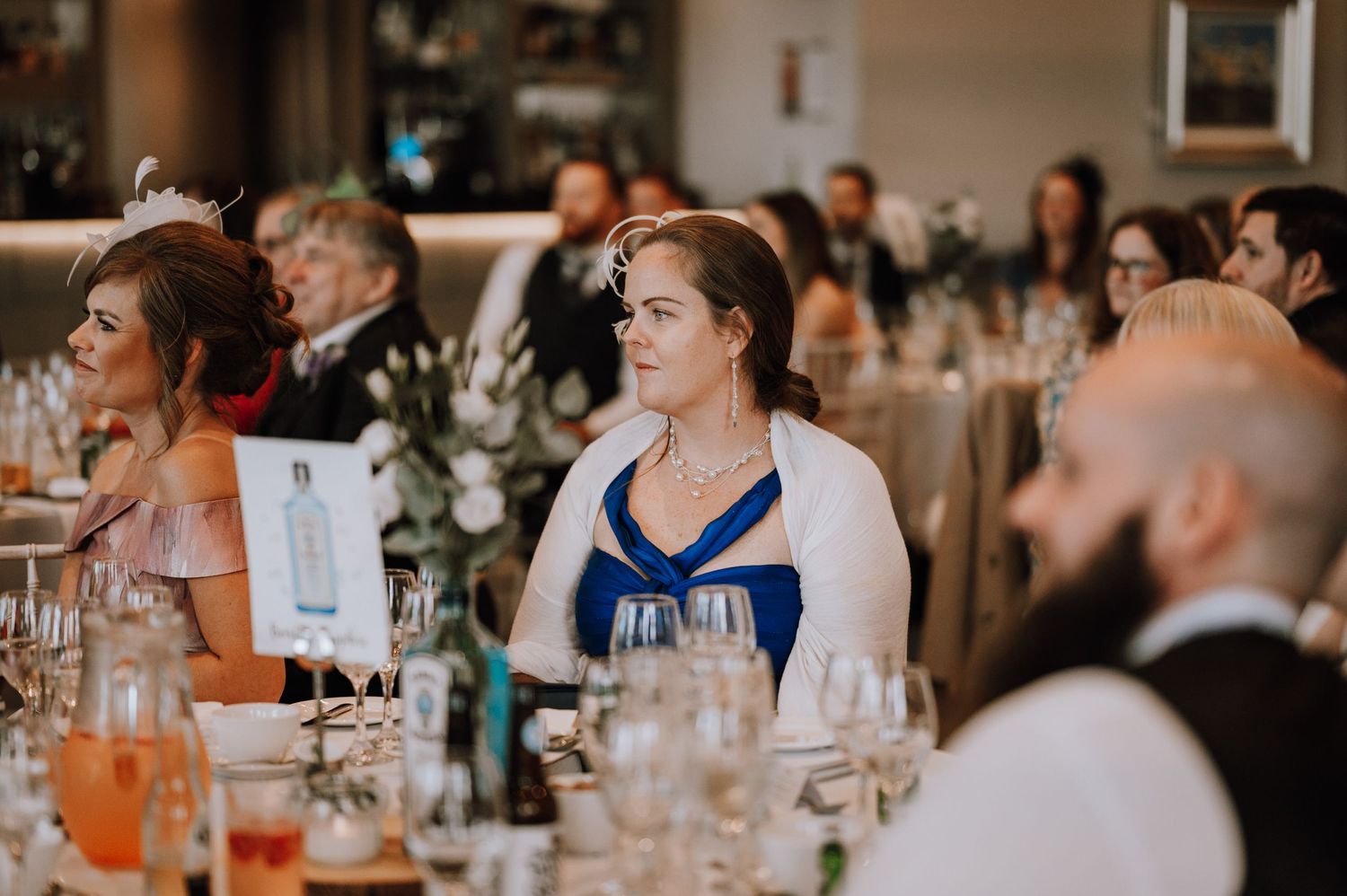 Guests seated at wedding reception tables with wine glasses and place settings.
