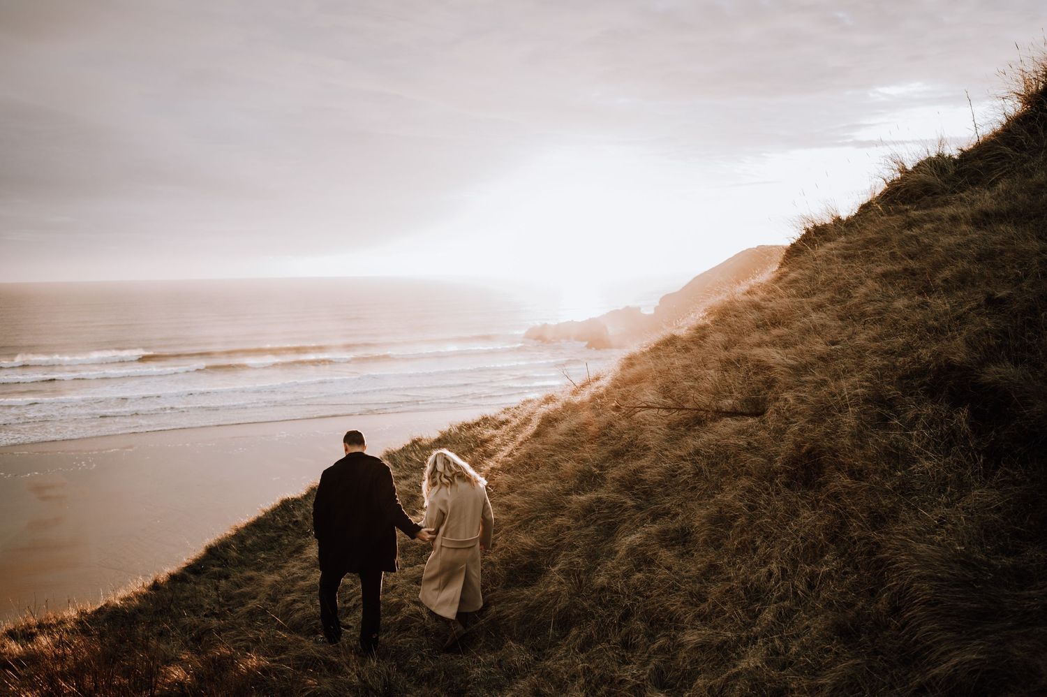 Silhouetted couple walking down coastal path during dramatic sunset.