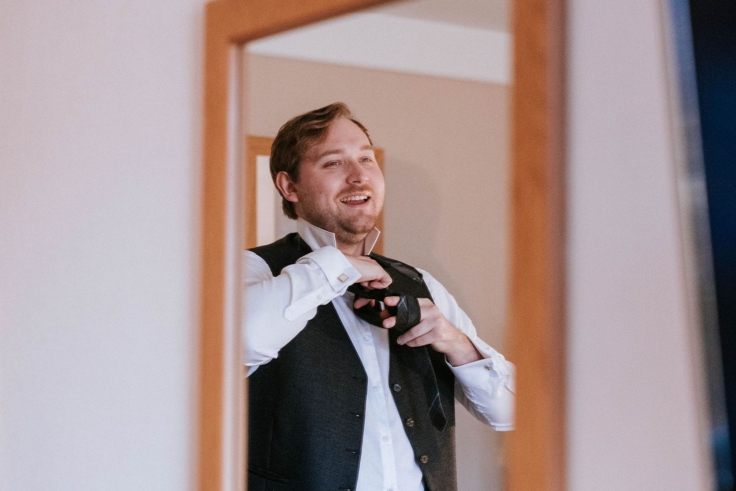Person in formal attire adjusting bowtie while getting ready in mirror reflection.
