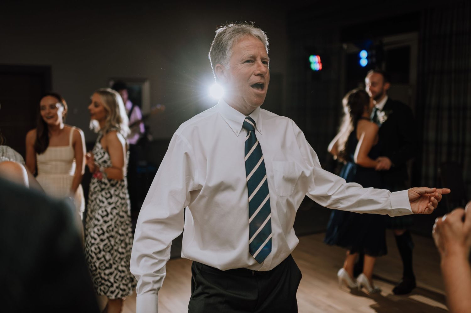 Man in formal attire enthusiastically dancing at an indoor event.