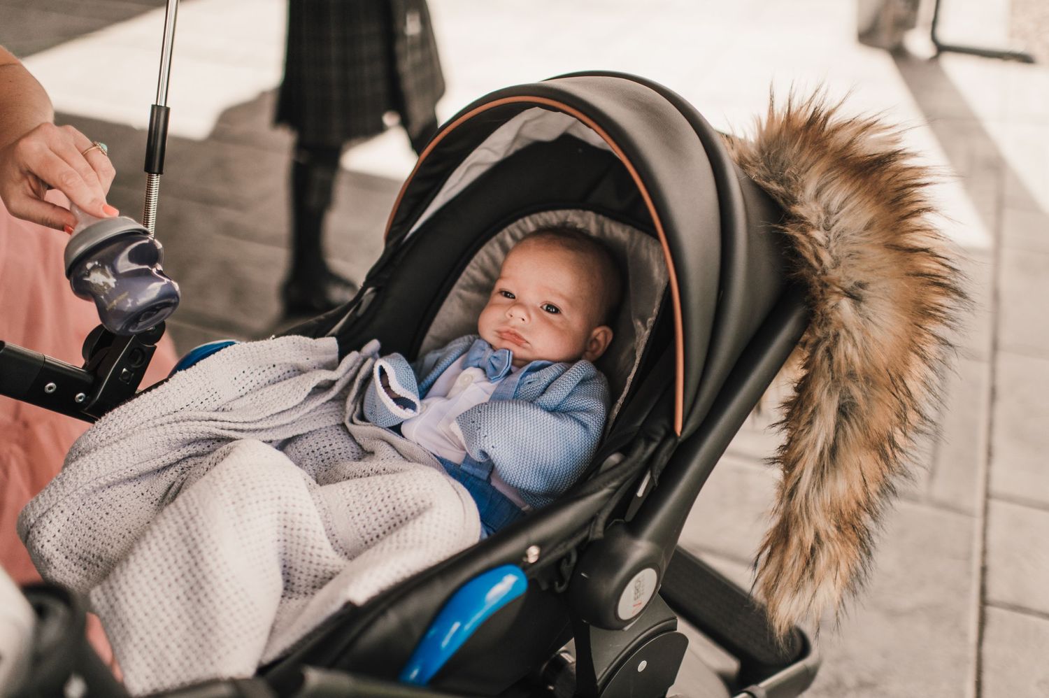 Smiling baby bundled in blanket sitting in stroller with fur-lined hood.