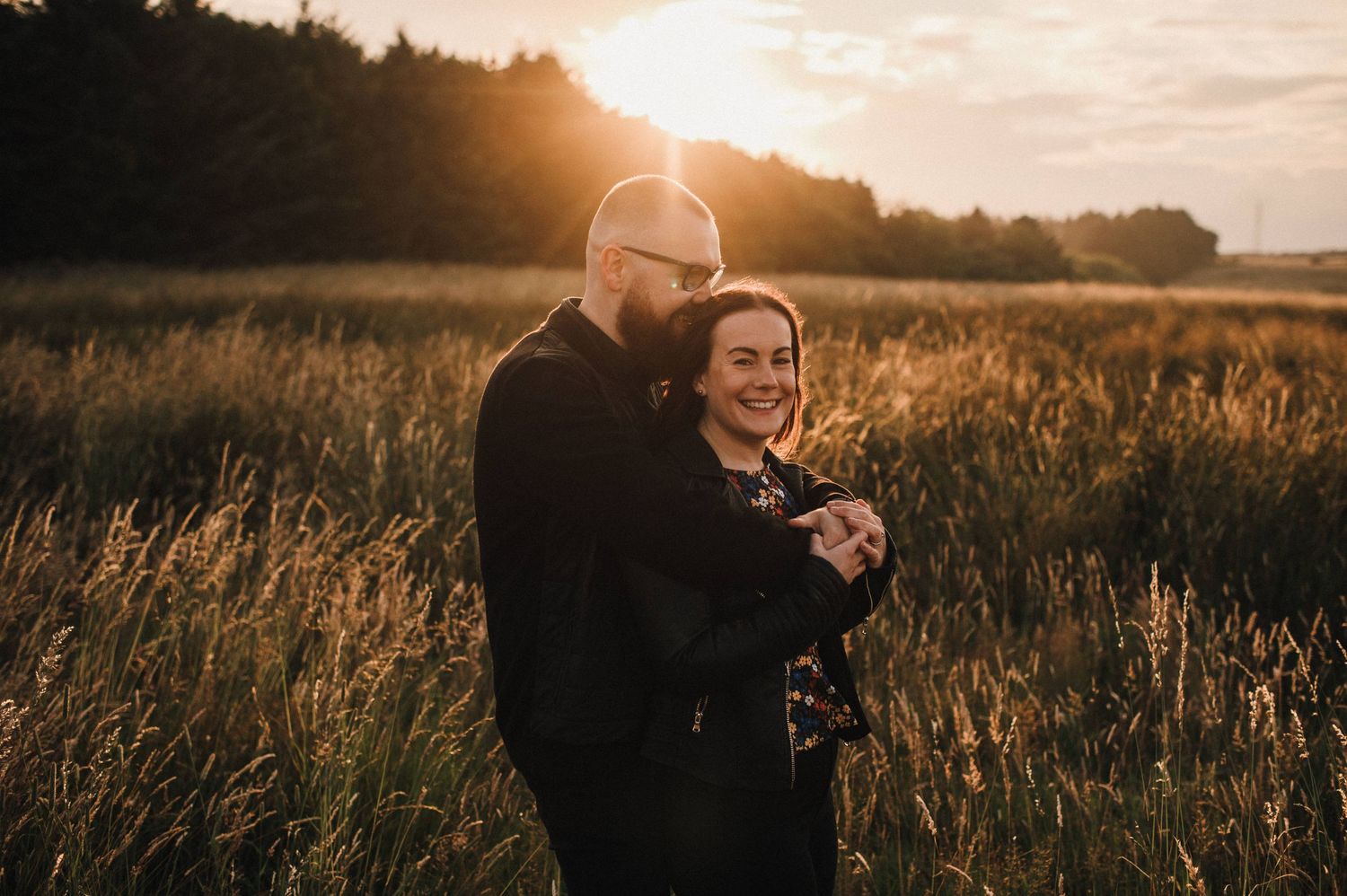 Joyful embrace captured in sunlit meadow with golden hour glow.
